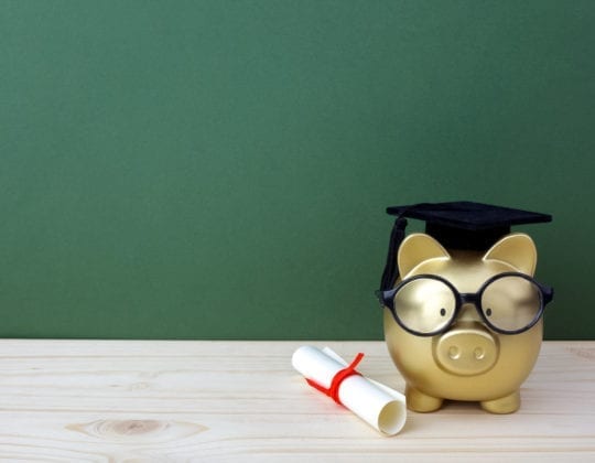 gold piggy bank wearing glasses and graduation cap with diploma