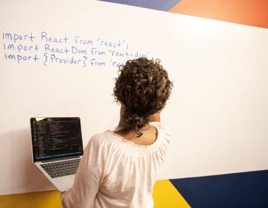 woman writing solution on whiteboard while holding laptop