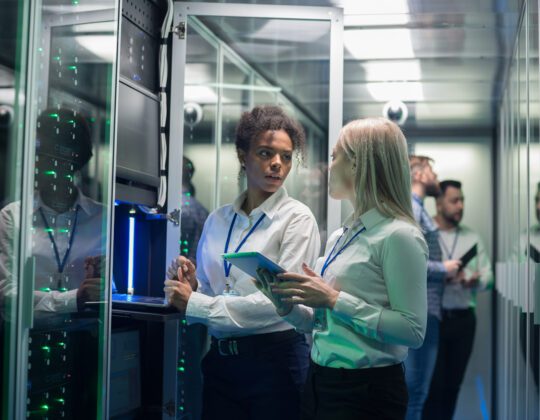 Two female cybersecurity professionals working between server stacks