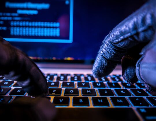 hands with gloves typing on computer to represent hacking of a computer